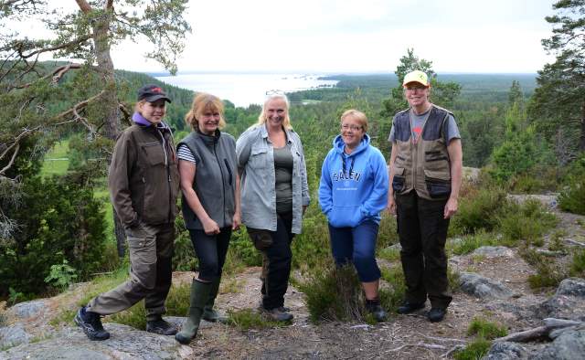 Fem kvinnor står på en höjd med en sjö i bakgrunden som kantas av bergs med skog